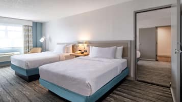 A hotel room with two beds, a desk, a lamp, and a window with curtains.