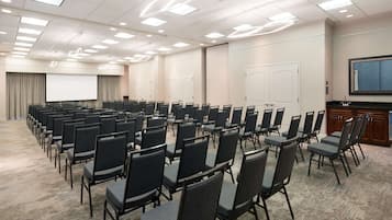 A conference room with rows of chairs, a projector screen, and a large screen on the wall.