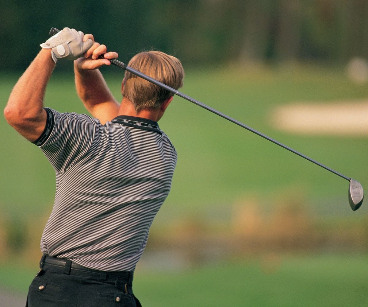 A golfer in a striped shirt and black pants swinging a golf club.