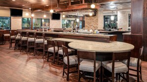 A bar area with wooden chairs, a round table, and a brick wall. - Hilton Garden Inn Jacksonville Ponte Vedra Sawgrass (Ponte Vedra Beach)