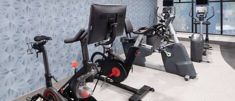 Un gimnasio con bicicletas estáticas, elípticas y un ventanal con vista a palmeras.