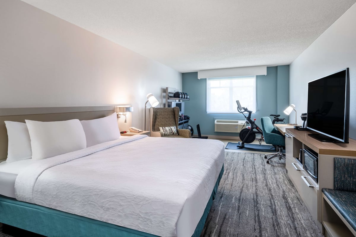 A hotel room with a large bed, a desk with a computer, a TV, and exercise equipment.