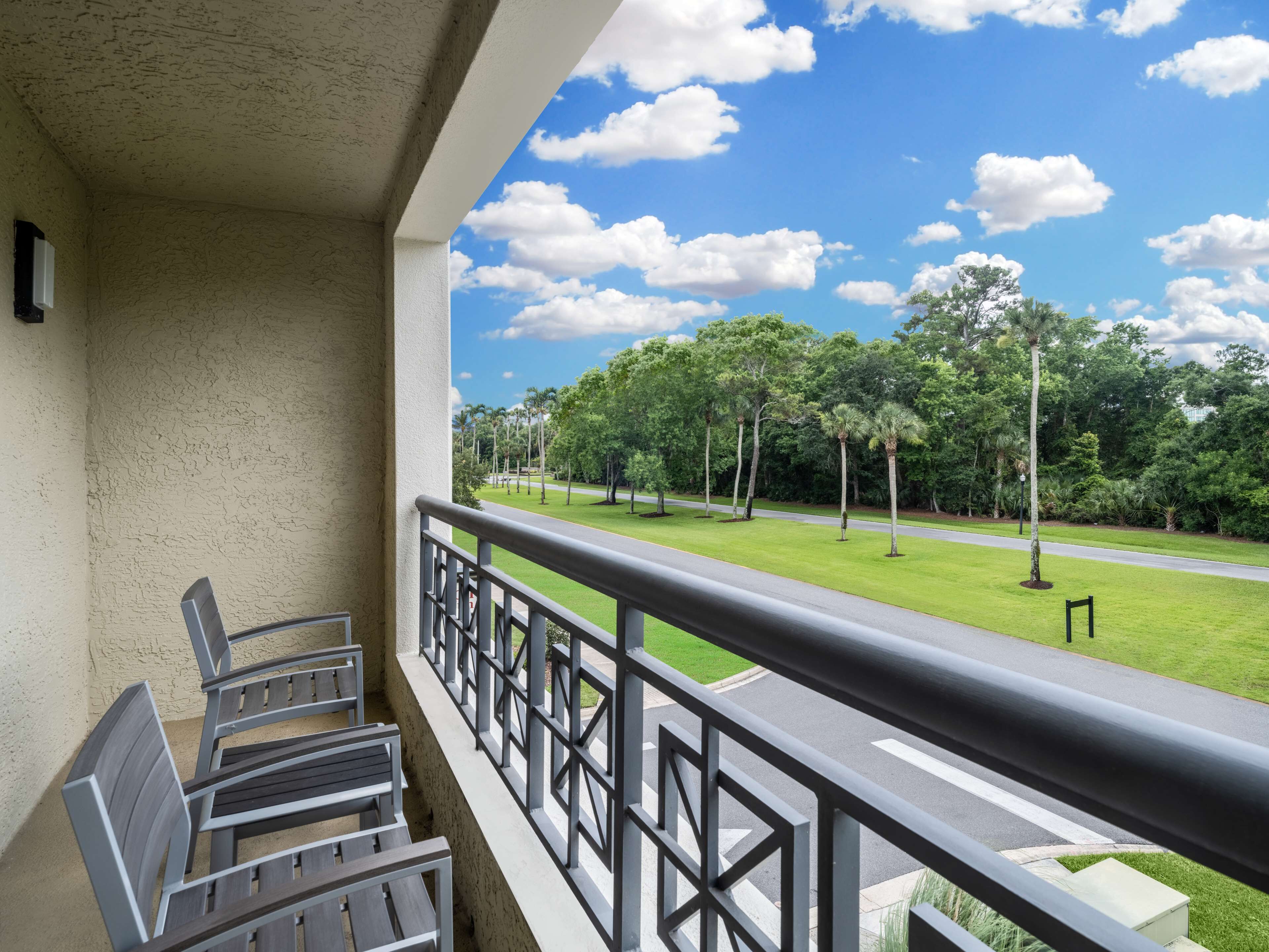 Un balcon donnant sur une pelouse bien entretenue et des arbres, avec une route pavée visible au loin.