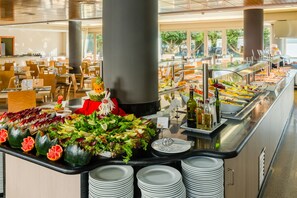 Zona de bufé con diversas opciones de comida, como ensaladas y frutas, en un amplio comedor con mesas y sillas.