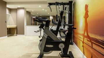Un gimnasio en casa con equipo de ejercicio, un espejo y una pared con un mural de atardecer.