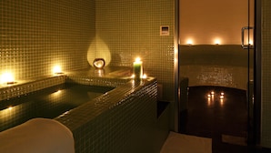 Un área de spa con hidromasaje, paredes con azulejos y velas que crean una iluminación ambiental.