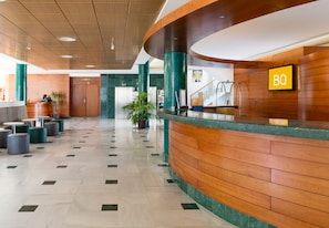 Un moderno vestíbulo de hotel con un mostrador de recepción curvo, una escalera y una planta grande en maceta.