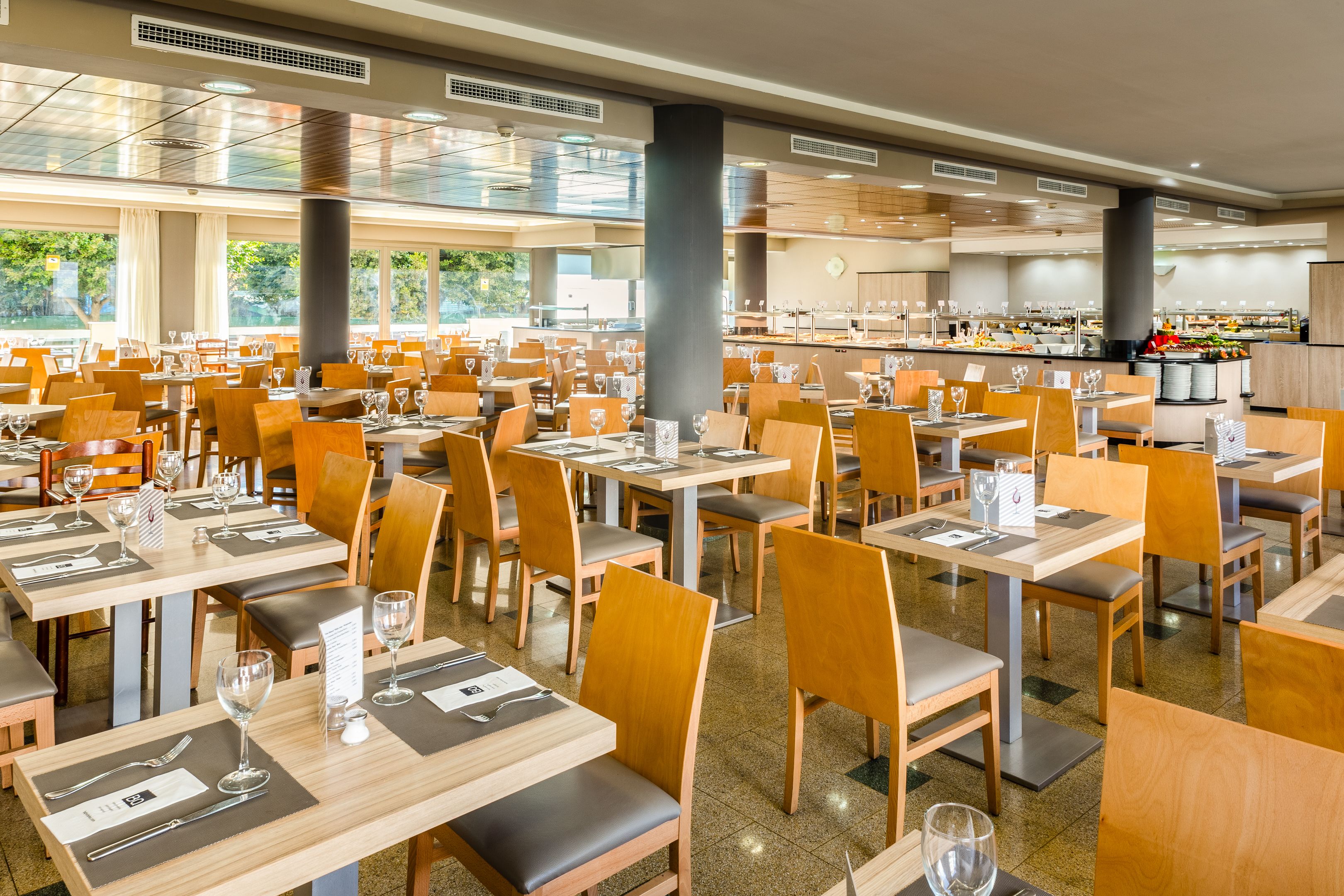 Ein geräumiges Restaurant mit mehreren Tischen und Stühlen, einer zentralen Bar und großen Fenstern mit Blick ins Freie.