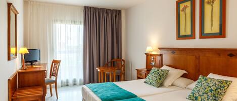 Ein Hotelzimmer mit einem großen Bett, einem Schreibtisch mit Computer, einem Sessel, einem Fernseher und einem Fenster mit Vorhängen.