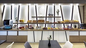 A breakfast bar with various food items and a coffee machine. There are two chairs and a table in the foreground. - ibis Styles A Coruña (A Coruña)