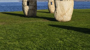 Three large stone sculptures on a grassy field with a clear blue sky and a body of water in the background. - ibis Styles A Coruña (A Coruña)