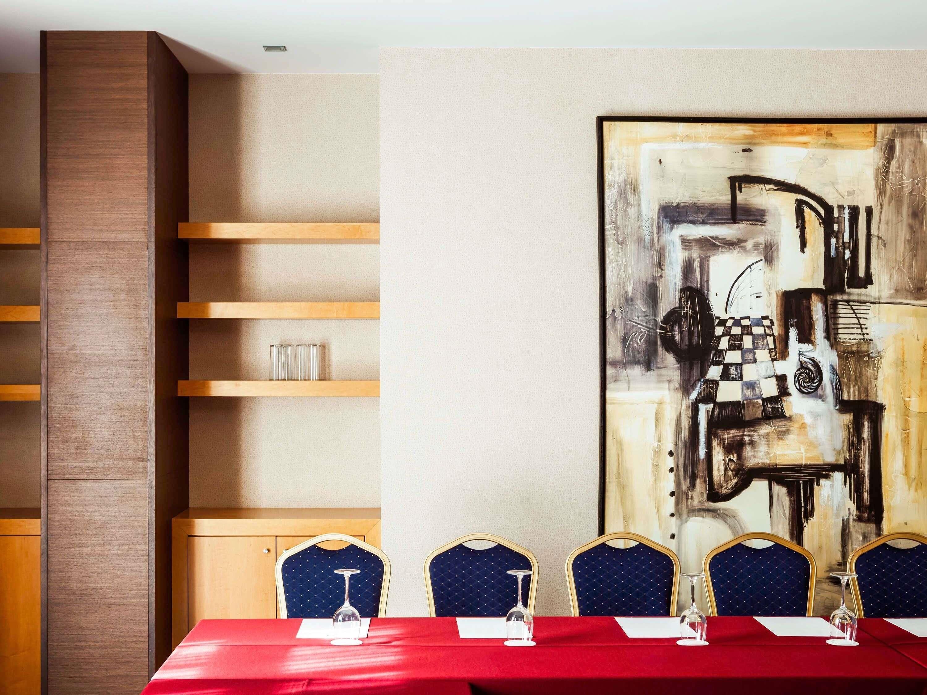 Un salón de conferencias con una mesa roja, sillas azules y un cuadro abstracto grande en la pared.