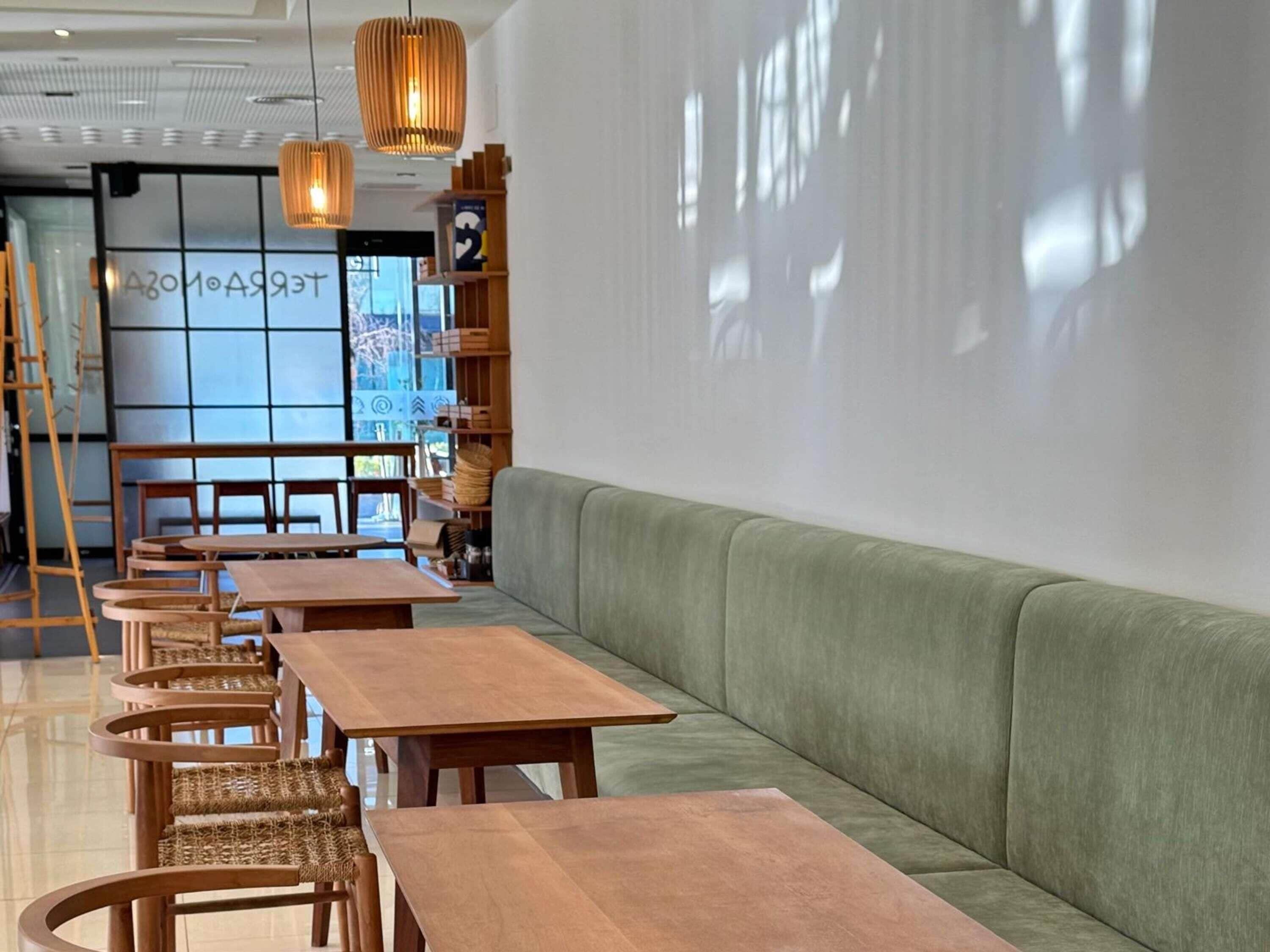 A modern interior with wooden tables and chairs, a green sofa, and hanging pendant lights.