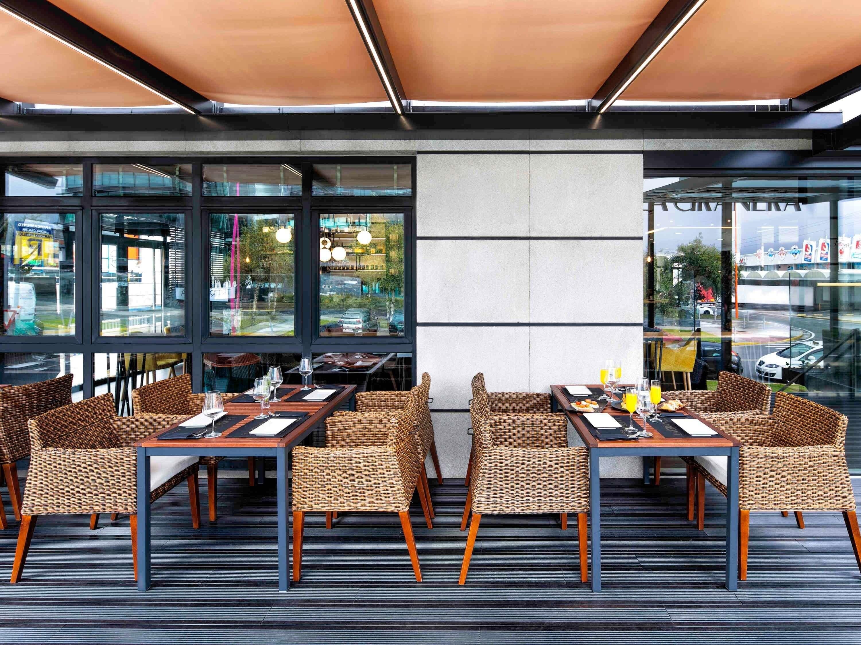 An outdoor dining area with wicker chairs and tables, large windows, and a view of the street.