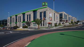 Hotel with a prominent sign, large windows, and a flat roof, situated on a street with a bike lane and palm trees.