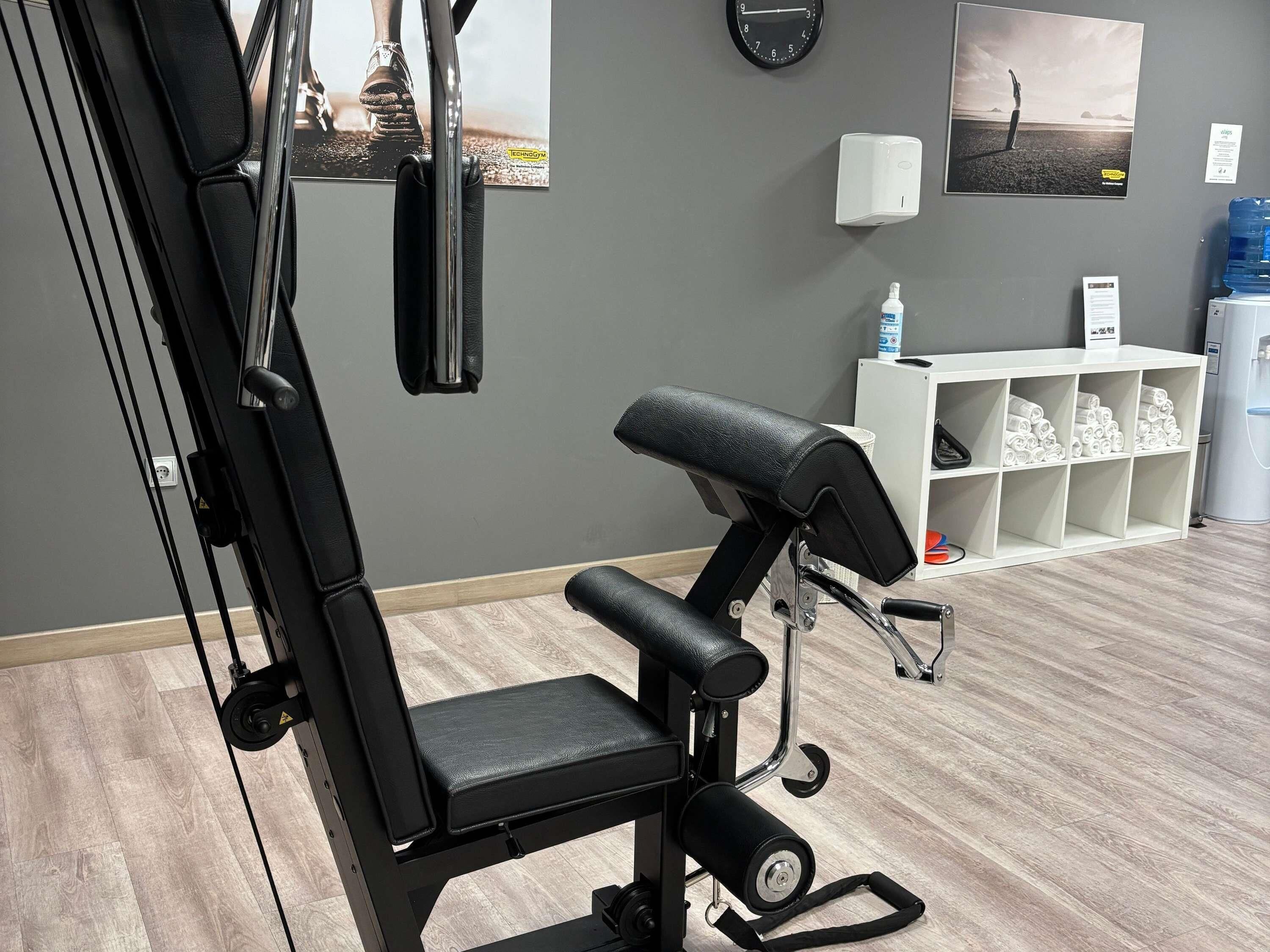 A gym with a bench press, wall-mounted clock, and a water dispenser.