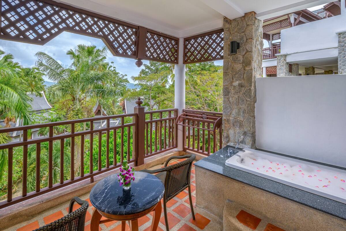 Un balcon orné d’un pilier en pierre, une table en marbre noir sur laquelle est posé un vase de fleurs, et une baignoire remplie de pétales de roses.