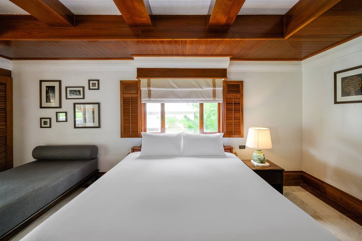 Une chambre avec un grand lit, une table de chevet avec une lampe, une fenêtre avec des volets et des tableaux encadrés accrochés au mur.
