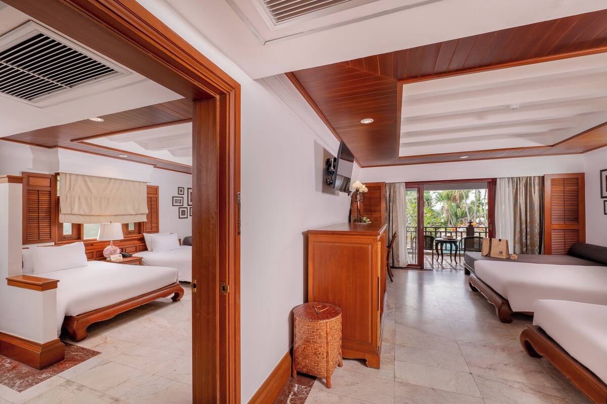 Une chambre d’hôtel avec un plafond en bois, un grand lit, un lit plus petit, un bureau et une vue sur l’extérieur.