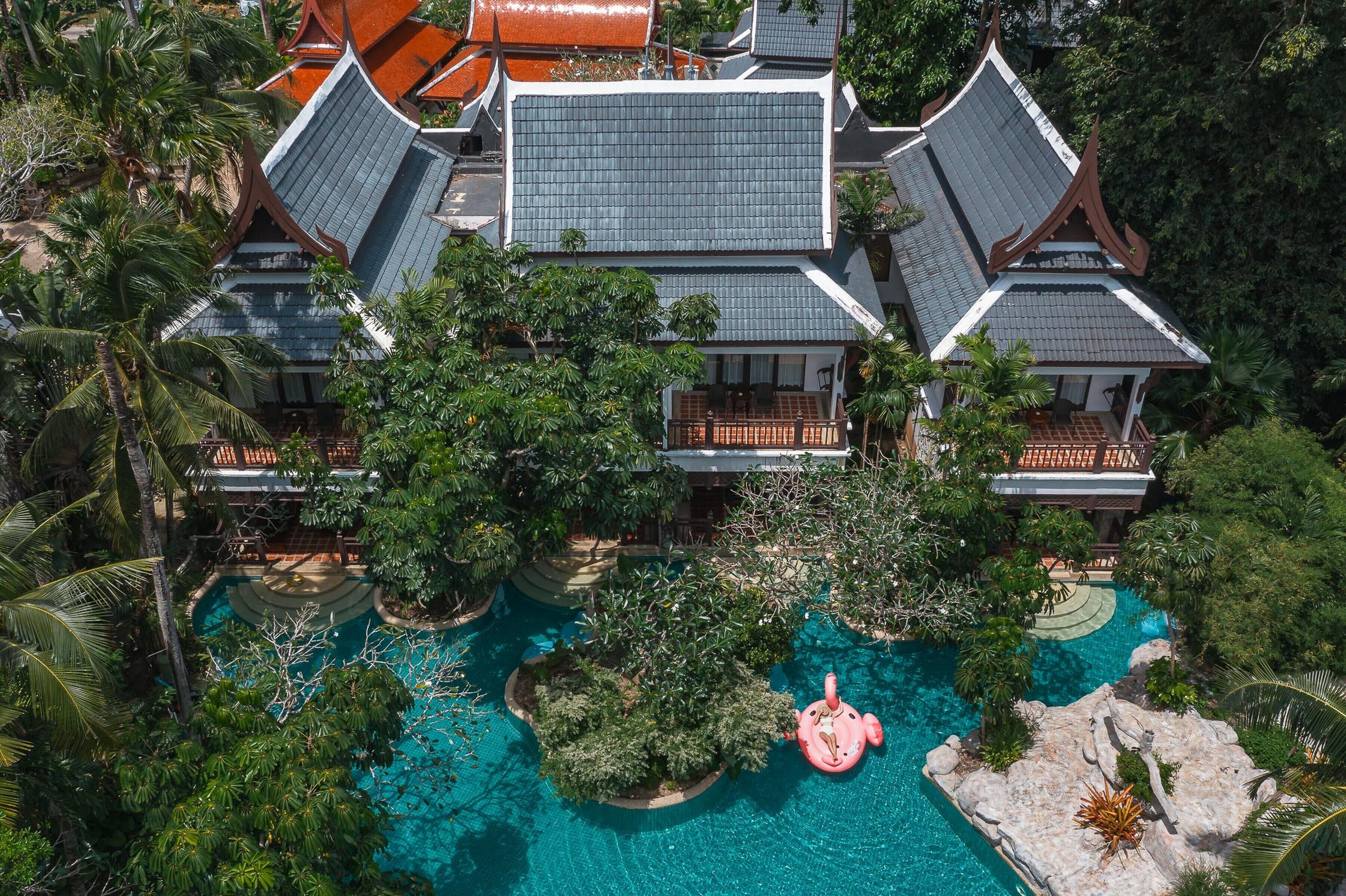 A large resort with multiple buildings, a central swimming pool, and lush greenery.