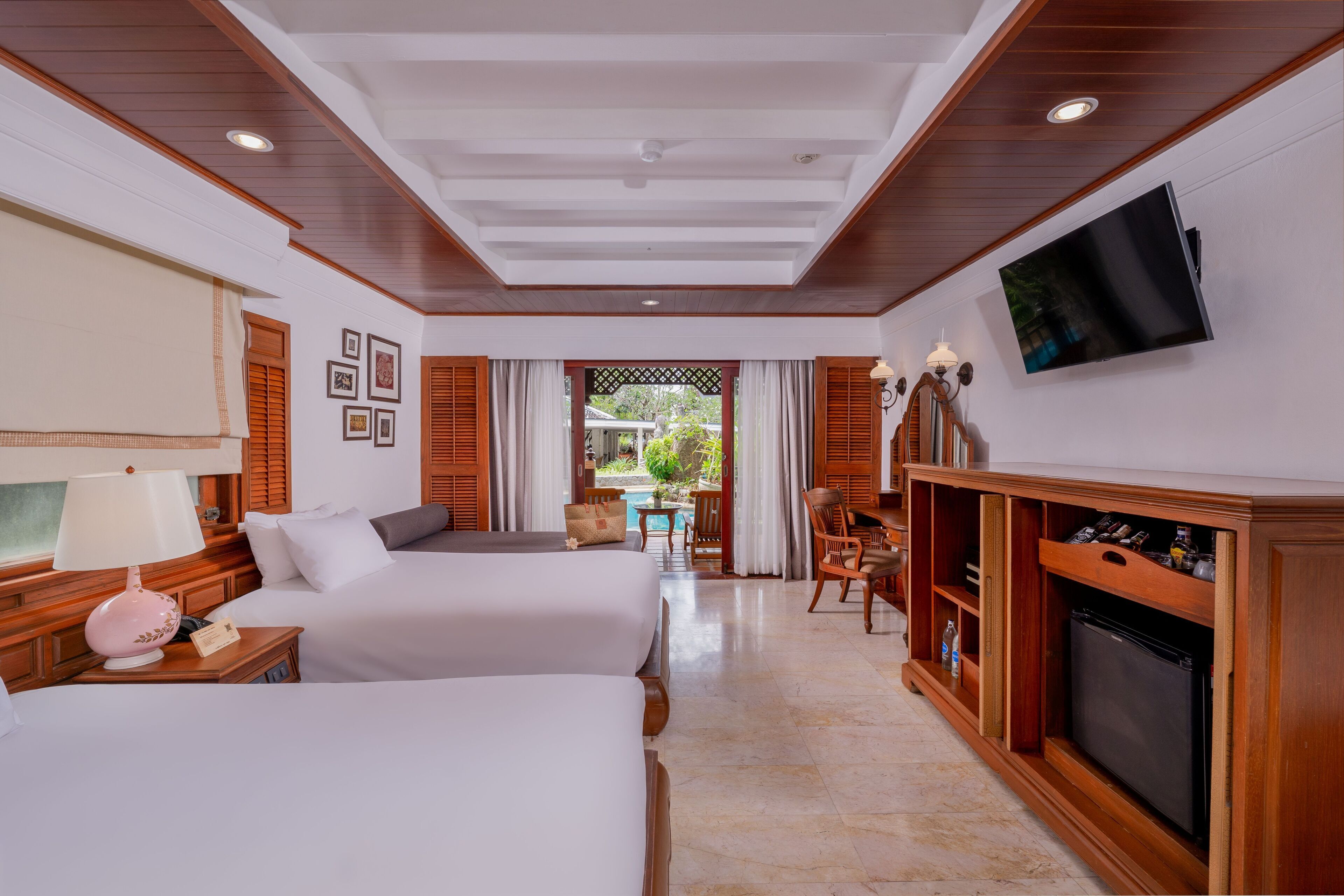 A hotel room with two beds, a TV, a wooden cabinet, and a view of the outdoors.