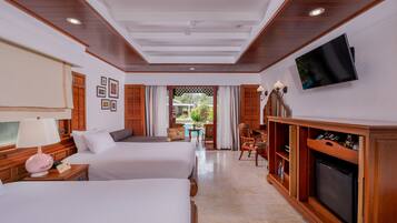A hotel room with two beds, a TV, a wooden cabinet, and a view of the outdoors.