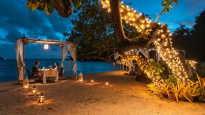 Un espace de restauration aménagé sur la plage, avec un auvent et des guirlandes lumineuses, offrant une vue sur la mer.