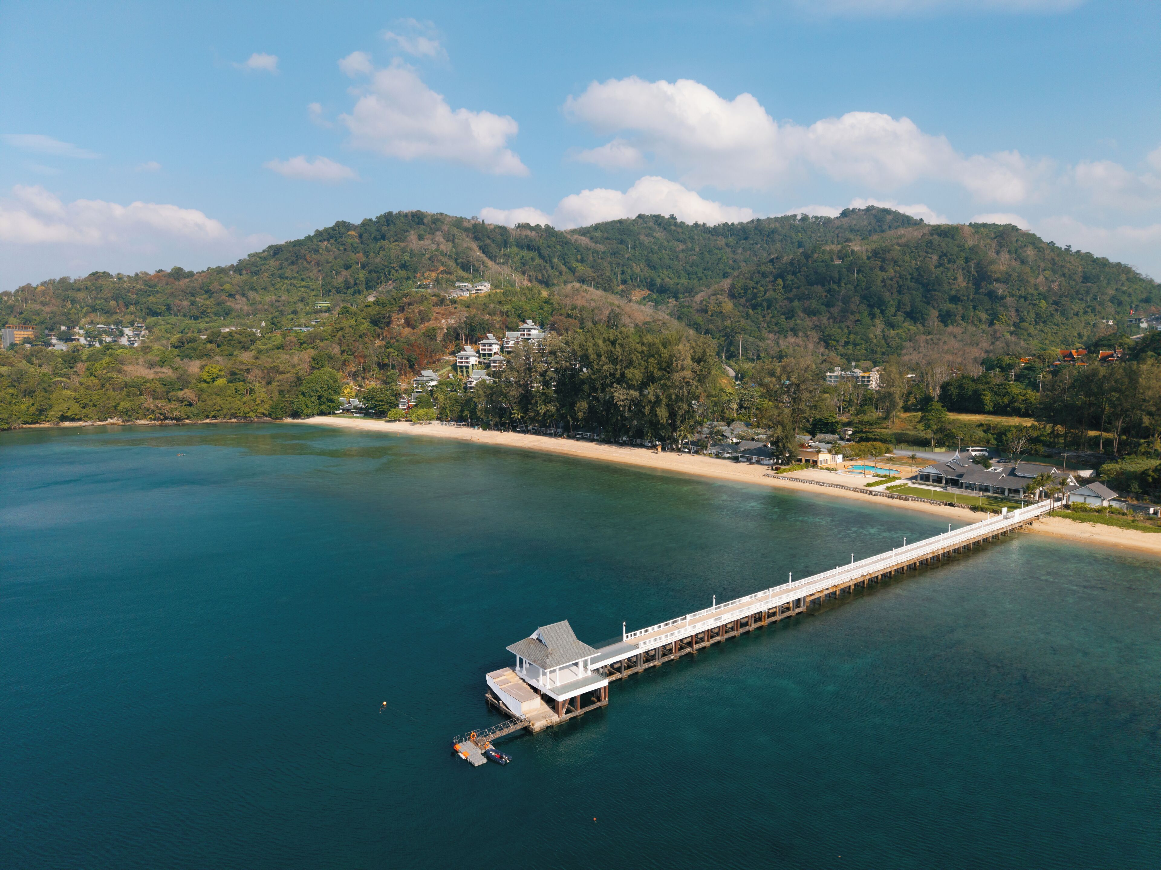 A coastal area with a long pier extending into the water, surrounded by hills and a beach.