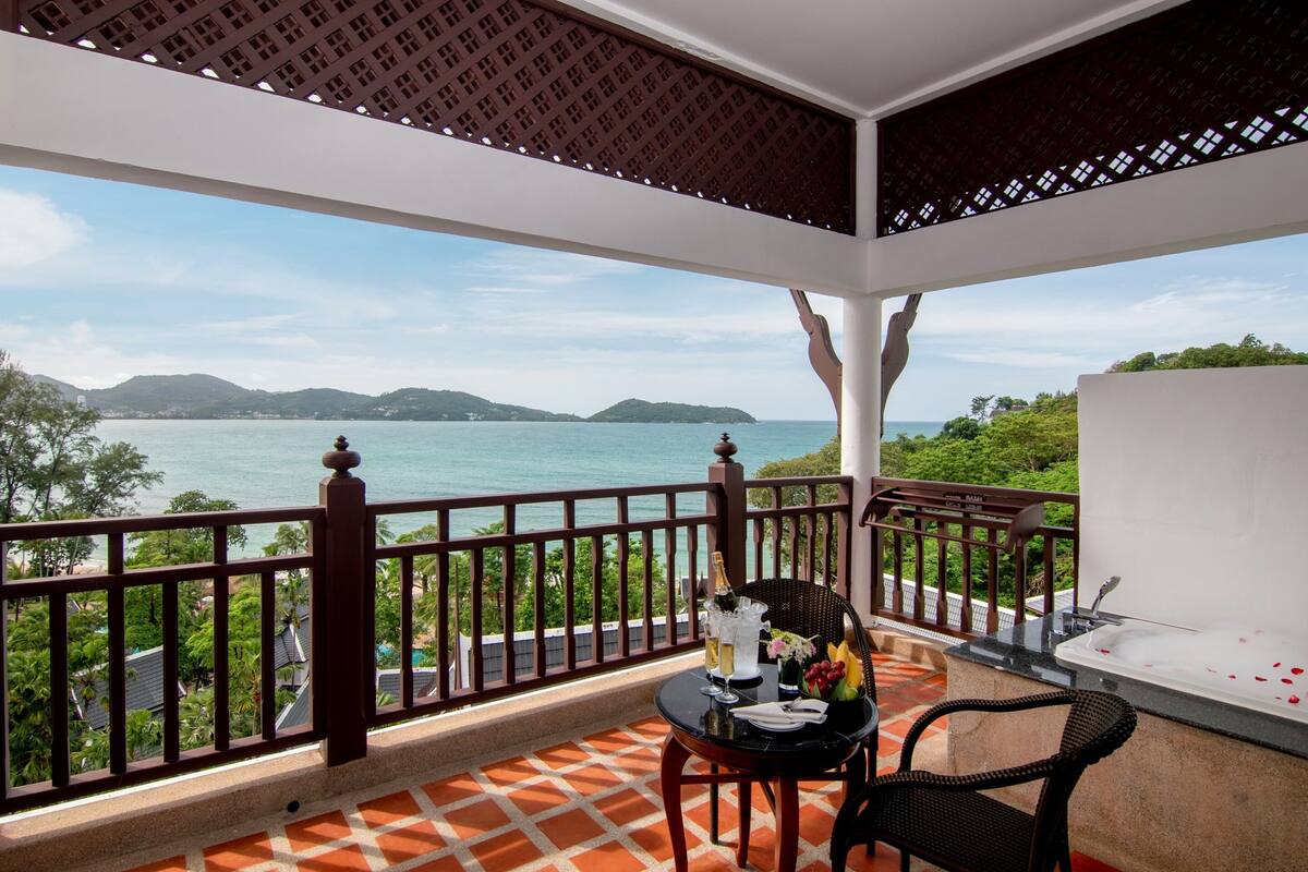 Un balcon avec vue sur la mer, une table avec une bouteille de champagne et une baignoire.