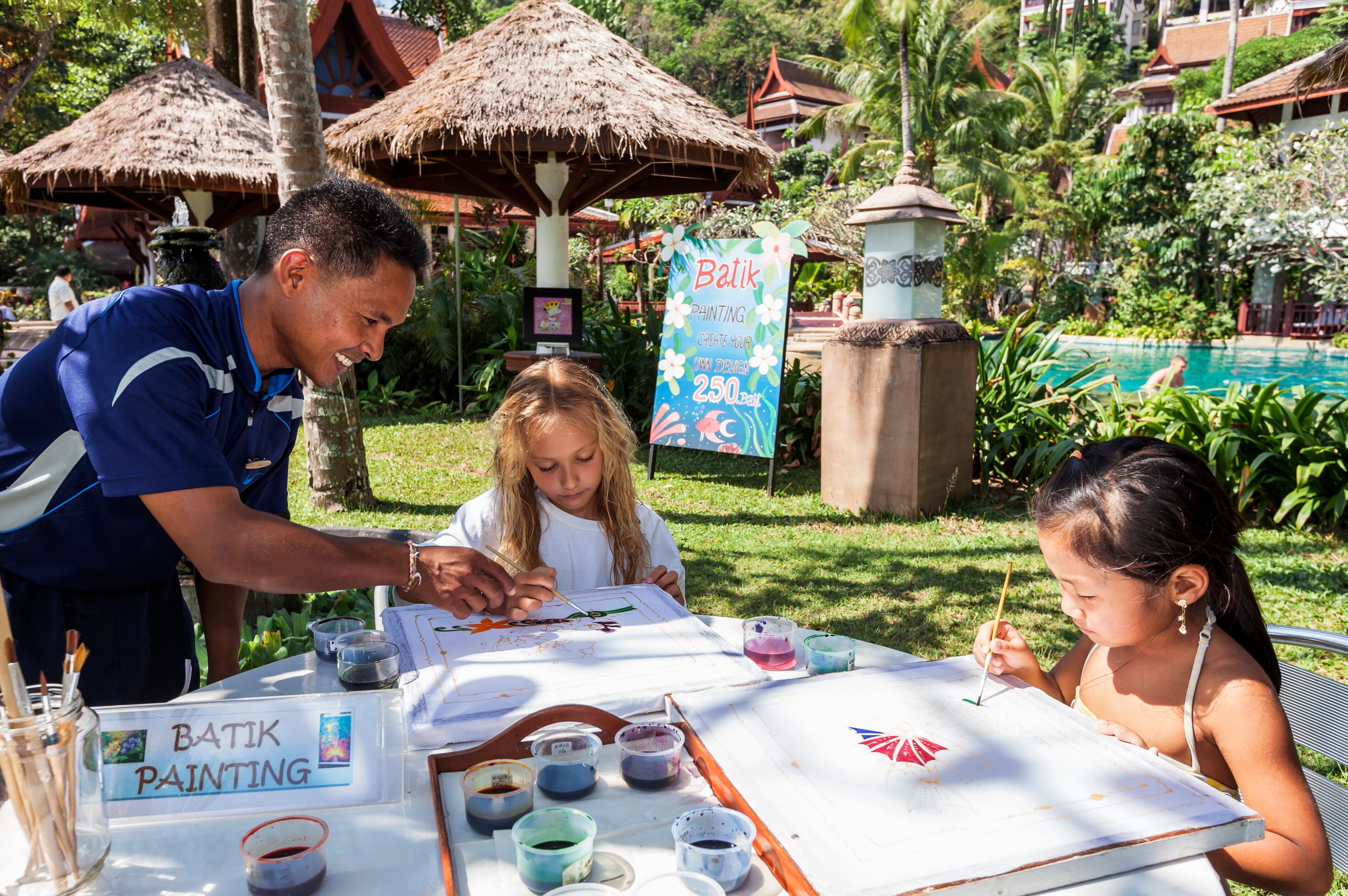 A painting activity setup with a table, painting supplies, and a sign for 'Batik Painting'.