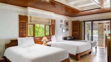 Une chambre d’hôtel avec deux lits, des têtes de lit en bois, une grande fenêtre avec volets, un mur en pierre et une vue sur la verdure environnante.