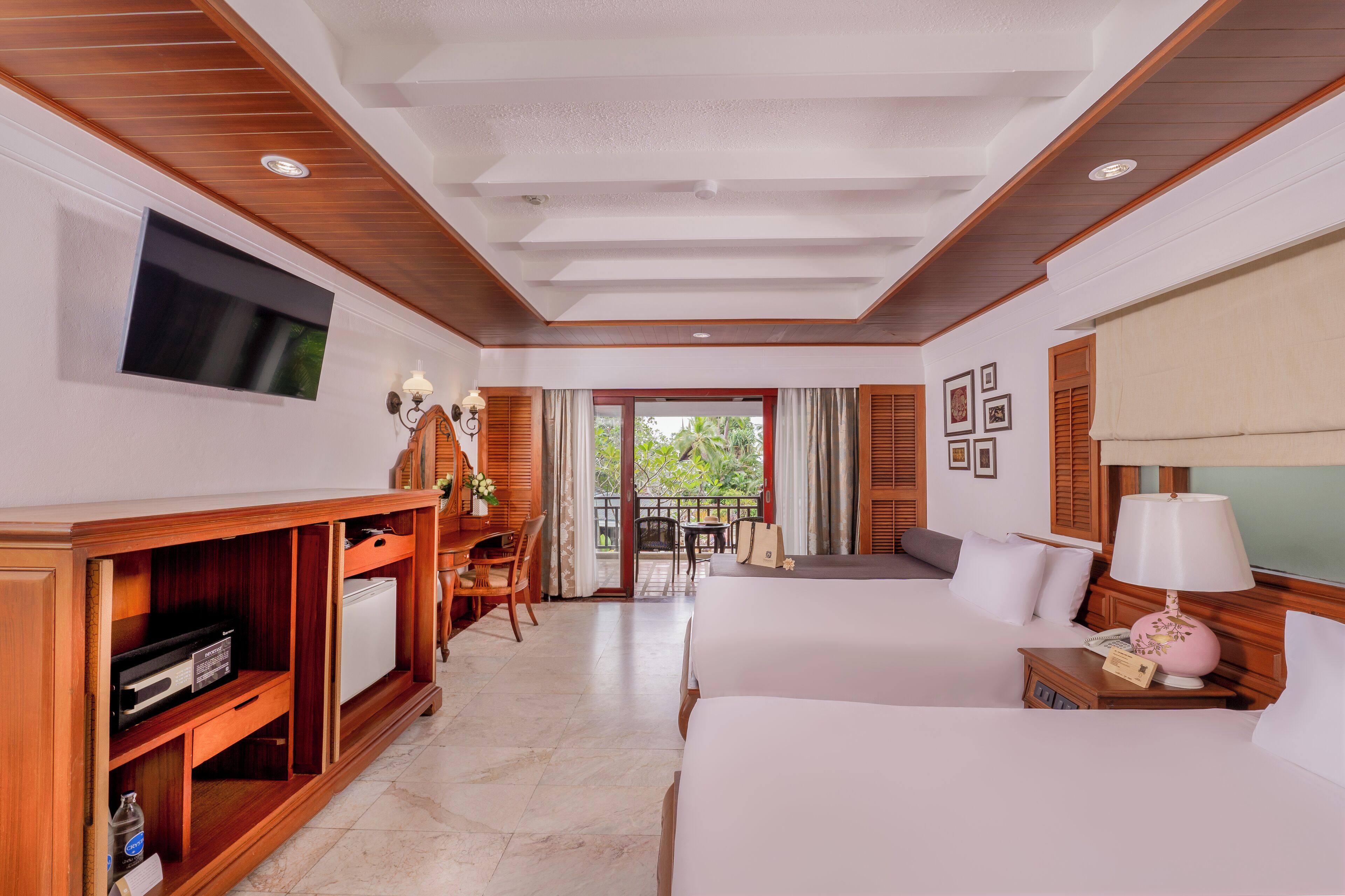 A hotel room with two beds, a TV, a desk with a chair, a small table, and a balcony with a view.