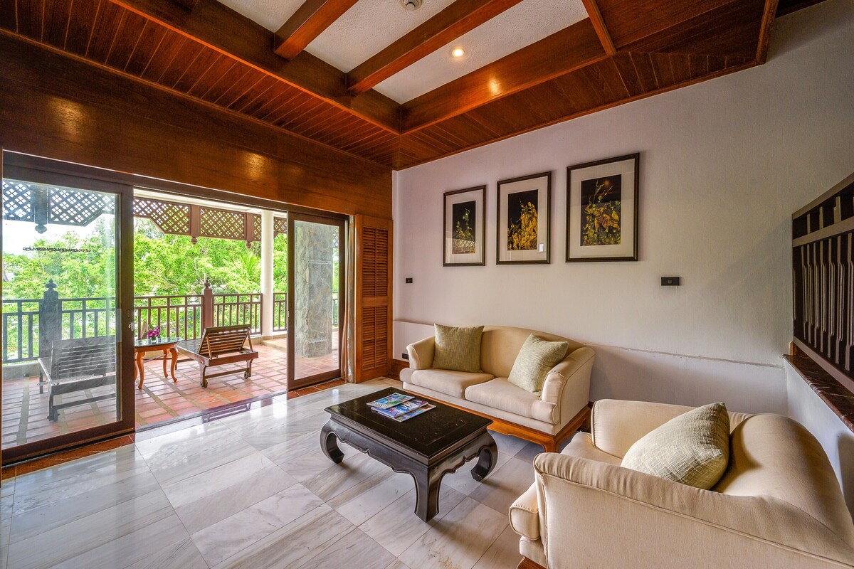 A spacious living area with a large sliding glass door leading to a balcony, a beige sofa, a coffee table, and framed artwork on the wall.