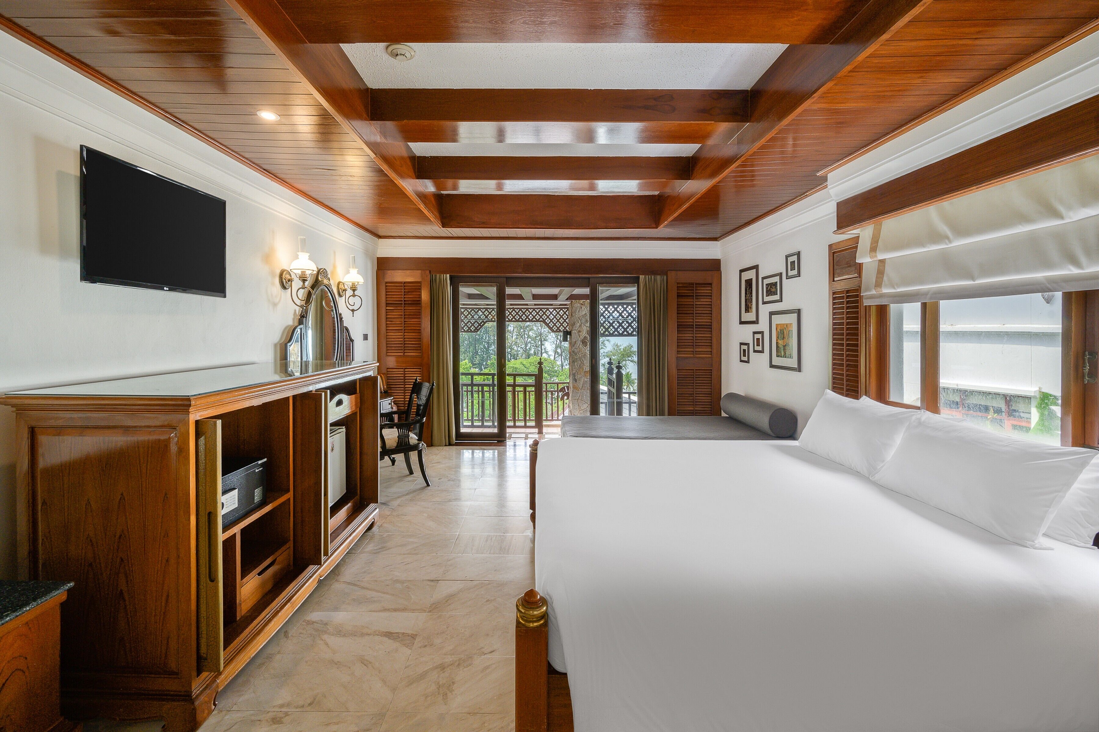 A hotel room with a large bed, wooden furniture, a flat-screen TV, and a balcony with a view.