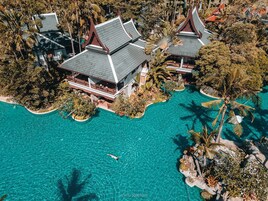 Vista aérea de un resort con varias construcciones de arquitectura tradicional, rodeado de aguas turquesas cristalinas y exuberante vegetación tropical.
