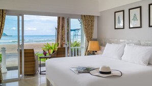 Een hotelkamer met een bed, nachtkastje, lamp en uitzicht op het strand en de oceaan.
