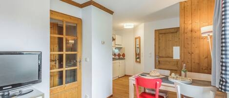 Una cocina moderna con armarios de madera, una zona de comedor con una silla roja y un televisor sobre un mueble blanco.