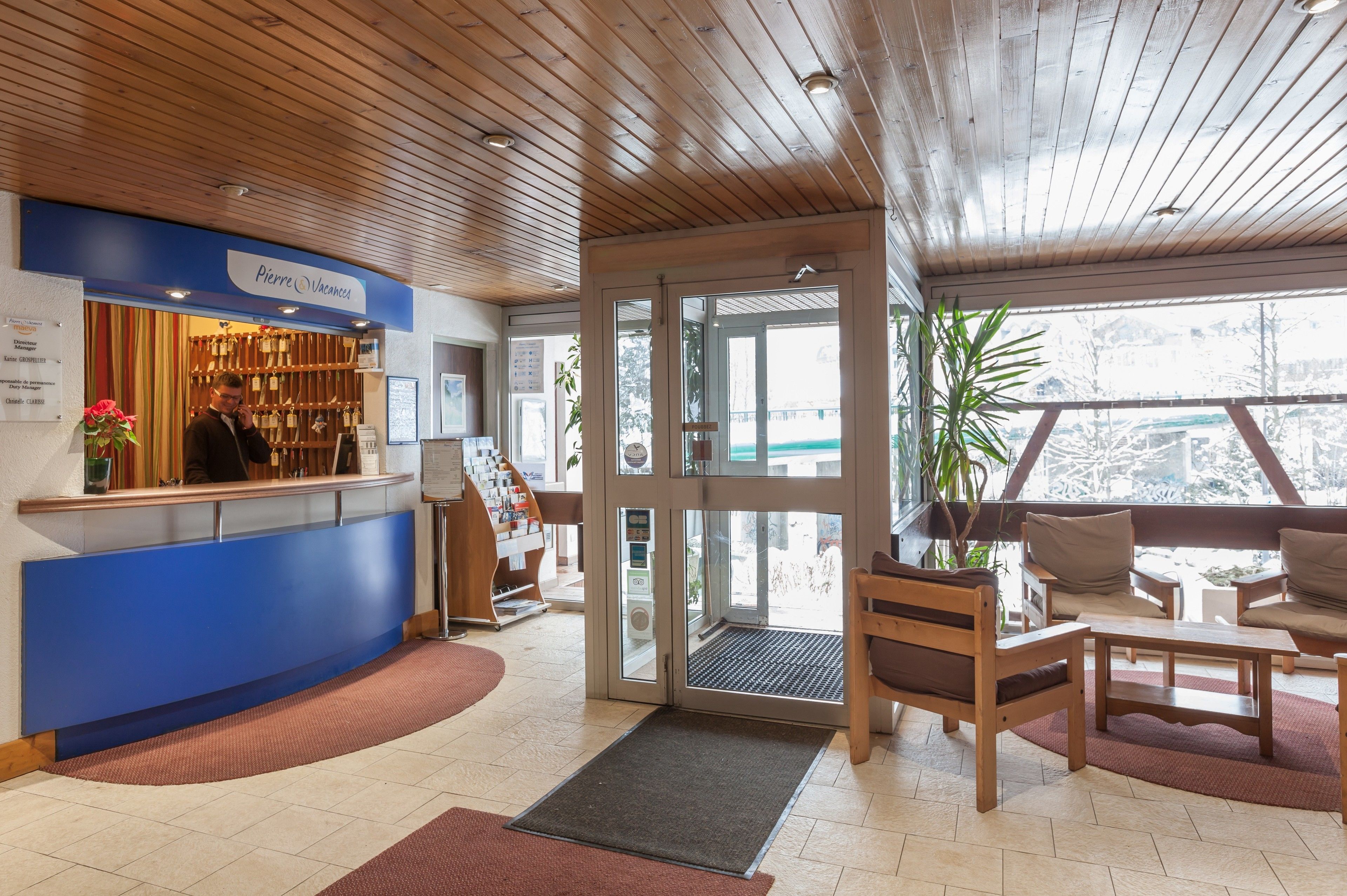 Un espace d’accueil doté d’un comptoir bleu, d’un plafond en bois et offrant une vue sur l’extérieur grâce à des portes vitrées.