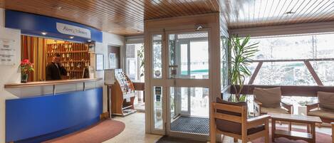 Un espace d’accueil doté d’un comptoir bleu, d’un plafond en bois et offrant une vue sur l’extérieur grâce à des portes vitrées.