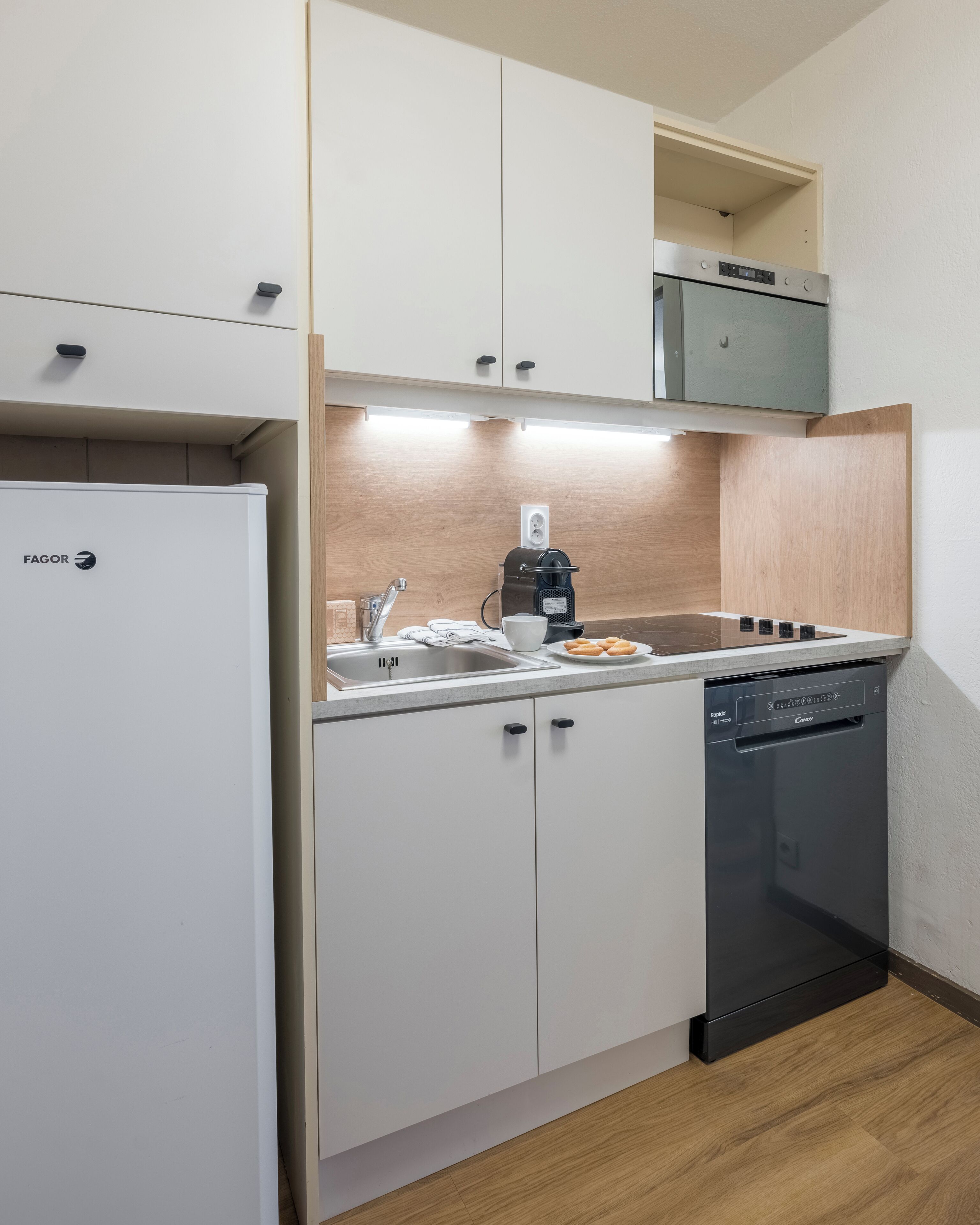 A compact kitchen with white cabinetry, a built-in oven, a coffee maker, and a dishwasher.