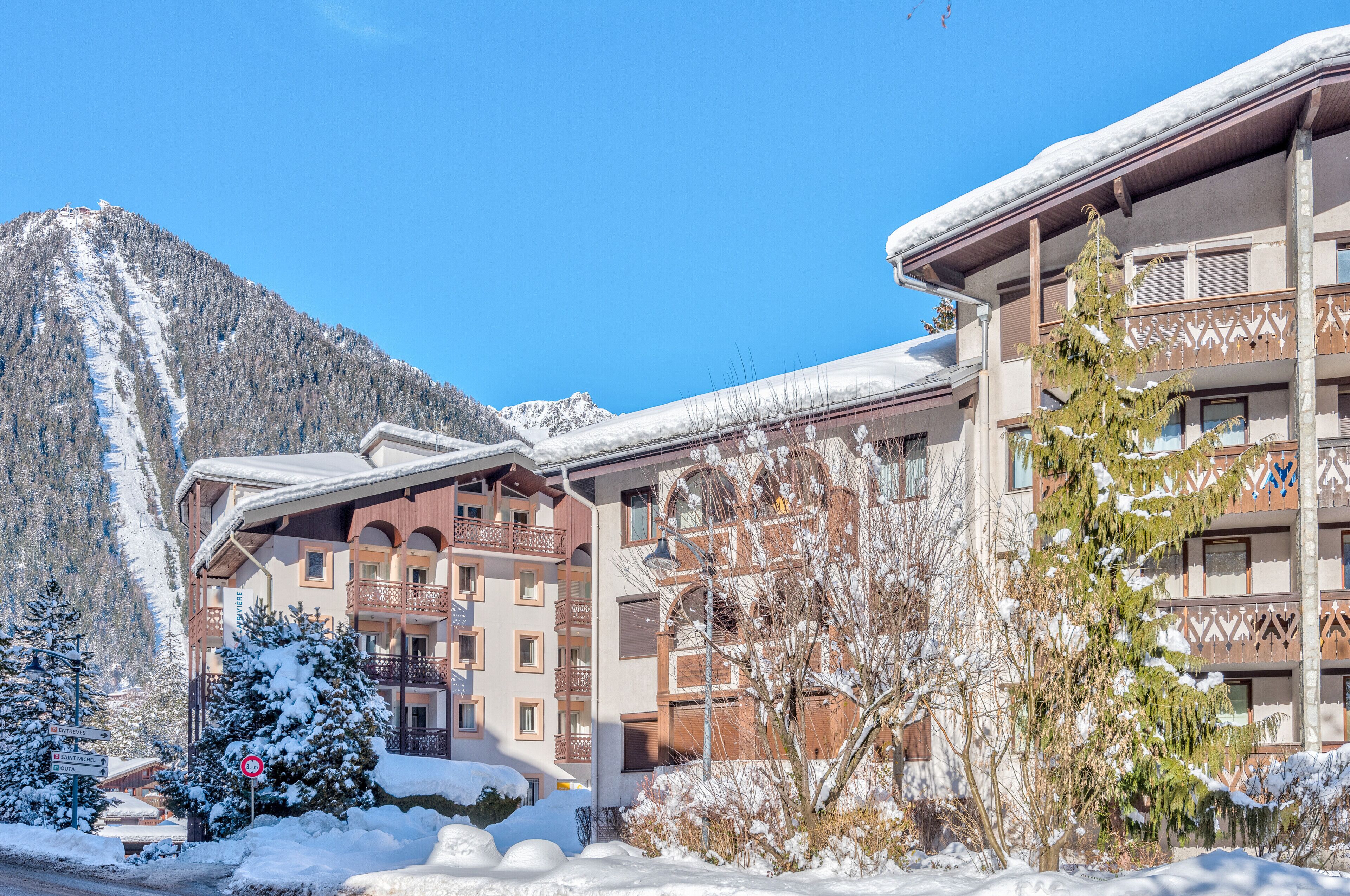 A multi-story building with balconies, snow-covered surroundings, and a mountainous backdrop.