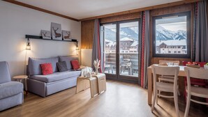 A modern living room with a grey sofa, wooden floor, and a dining area with a table and chairs. - Résidence Pierre & Vacances Chamonix La Rivière (Chamonix-Mont-Blanc)