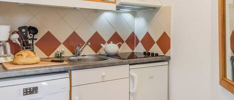 Een kleine keuken met witte kastjes, een magnetron, een spoelbak en een houten aanrecht.