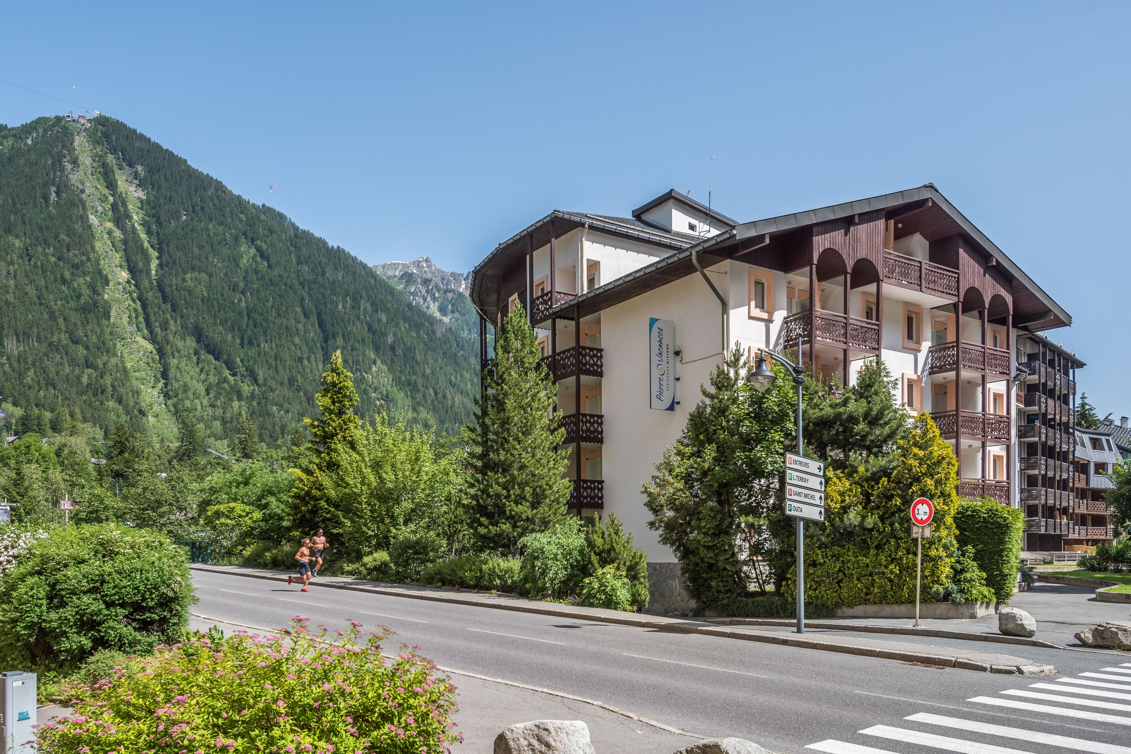 A hotel with a balcony, surrounded by greenery and mountains.