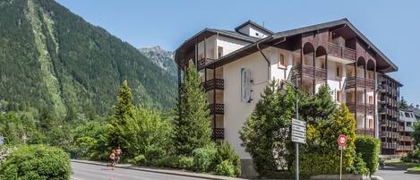 A hotel with a balcony, surrounded by greenery and mountains.