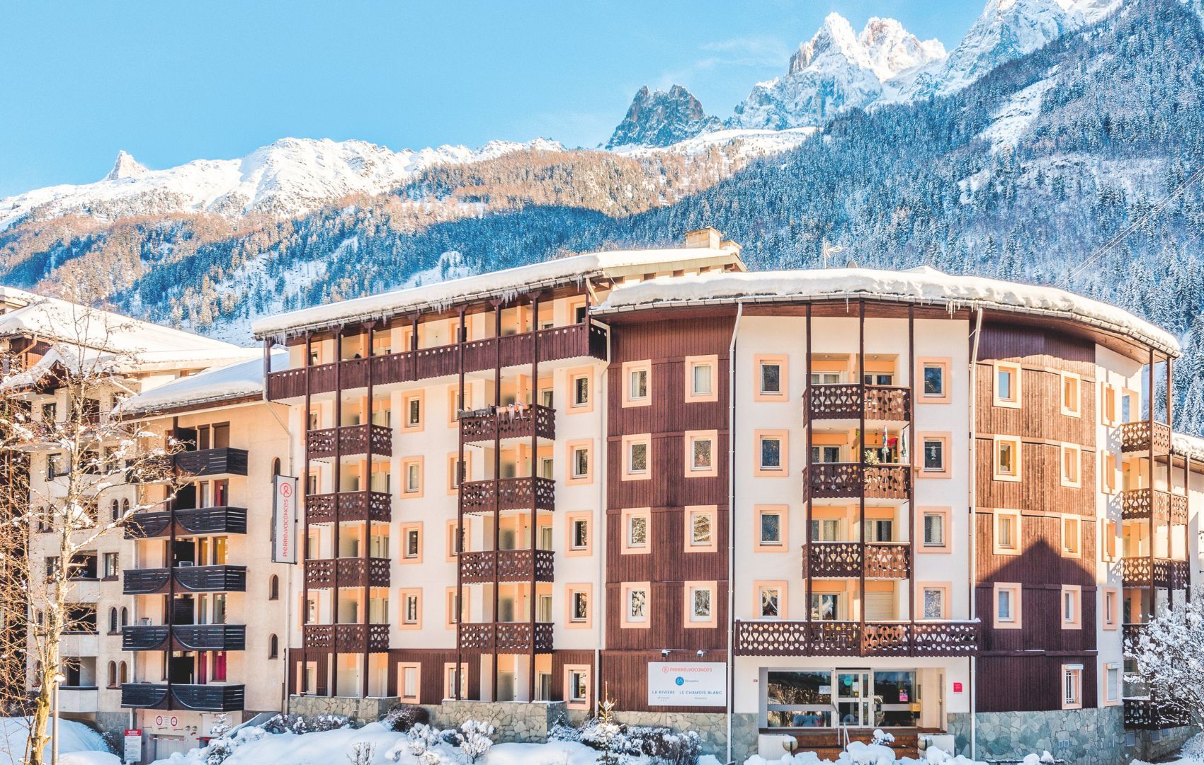 A multi-story hotel with balconies, set against a snowy mountain backdrop.