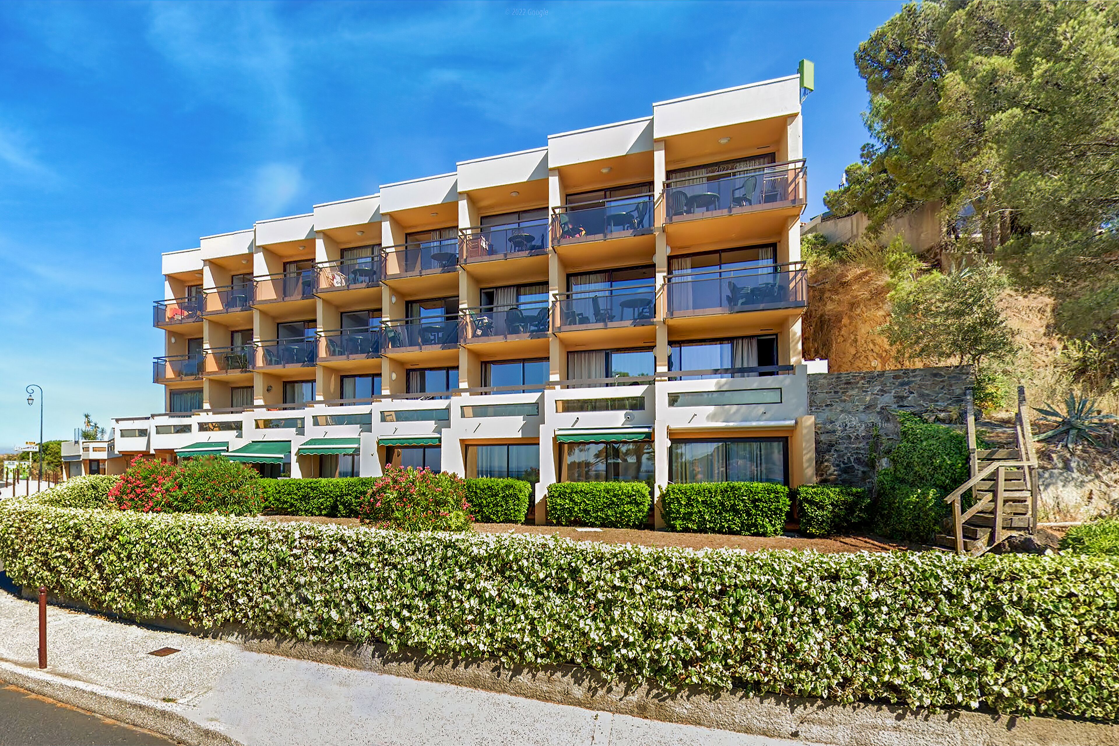 A multi-story hotel with balconies, a stone facade, and a well-maintained garden.