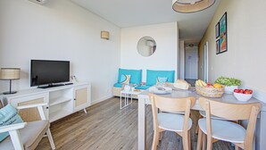 A modern living room with a flat-screen TV, a sofa with blue cushions, a dining table with chairs, and a basket of fruit. - Pierre & Vacances Résidence Les Balcons de Collioure (Collioure)