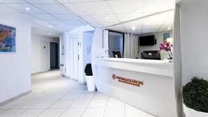 A clean, modern reception area with a white reception desk, a flat-screen TV, and a potted plant. - Pierre & Vacances Résidence Les Balcons de Collioure (Collioure)
