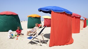 Una playa con sombrillas de colores y una persona sentada en una silla de playa.